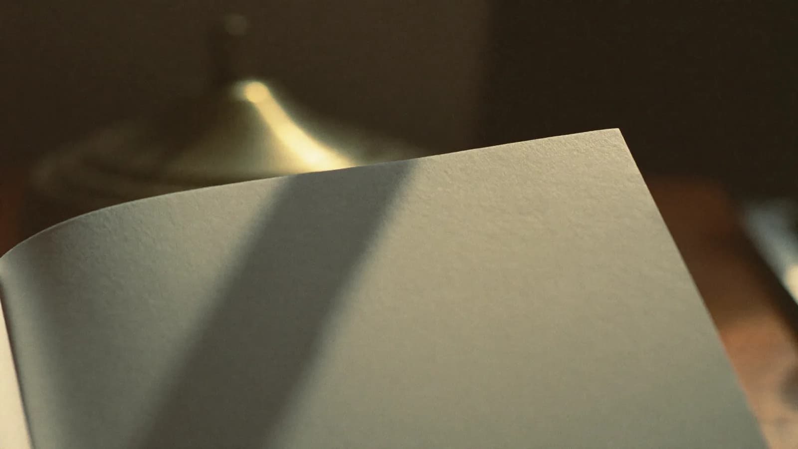The corner of a blank sheet of script paper on a walnut desk in low golden hour light, cinematic still