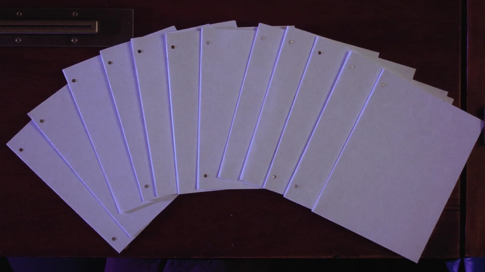 Several screenplay title pages fanned out on a dark studio desk, overhead cinematic still