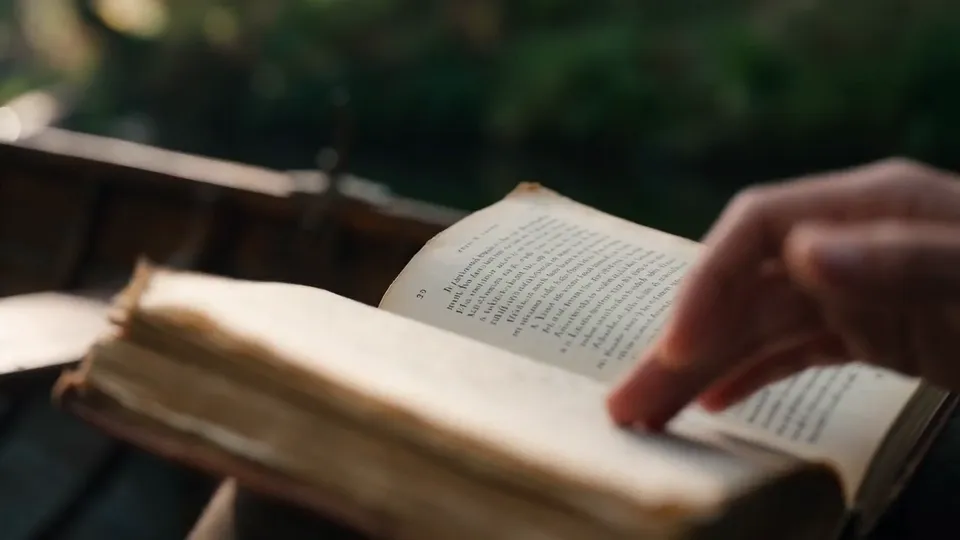 A hand turning the yellowed page of an old book in a wooden rowboat