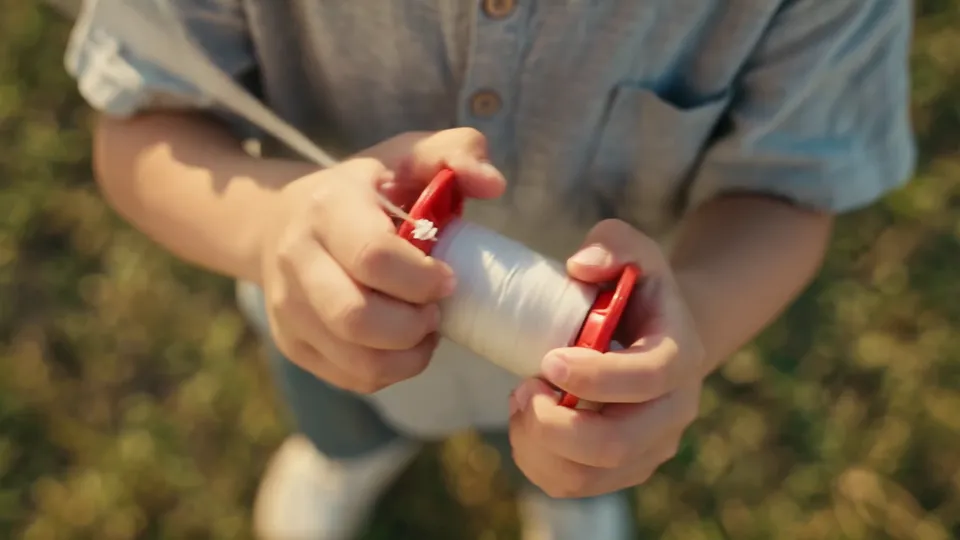 A child's hands gripping a red kite spool as white string unwinds