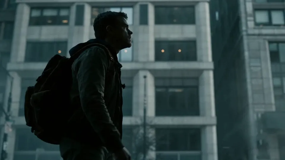 A man with a backpack in profile looks up in front of a grey office building